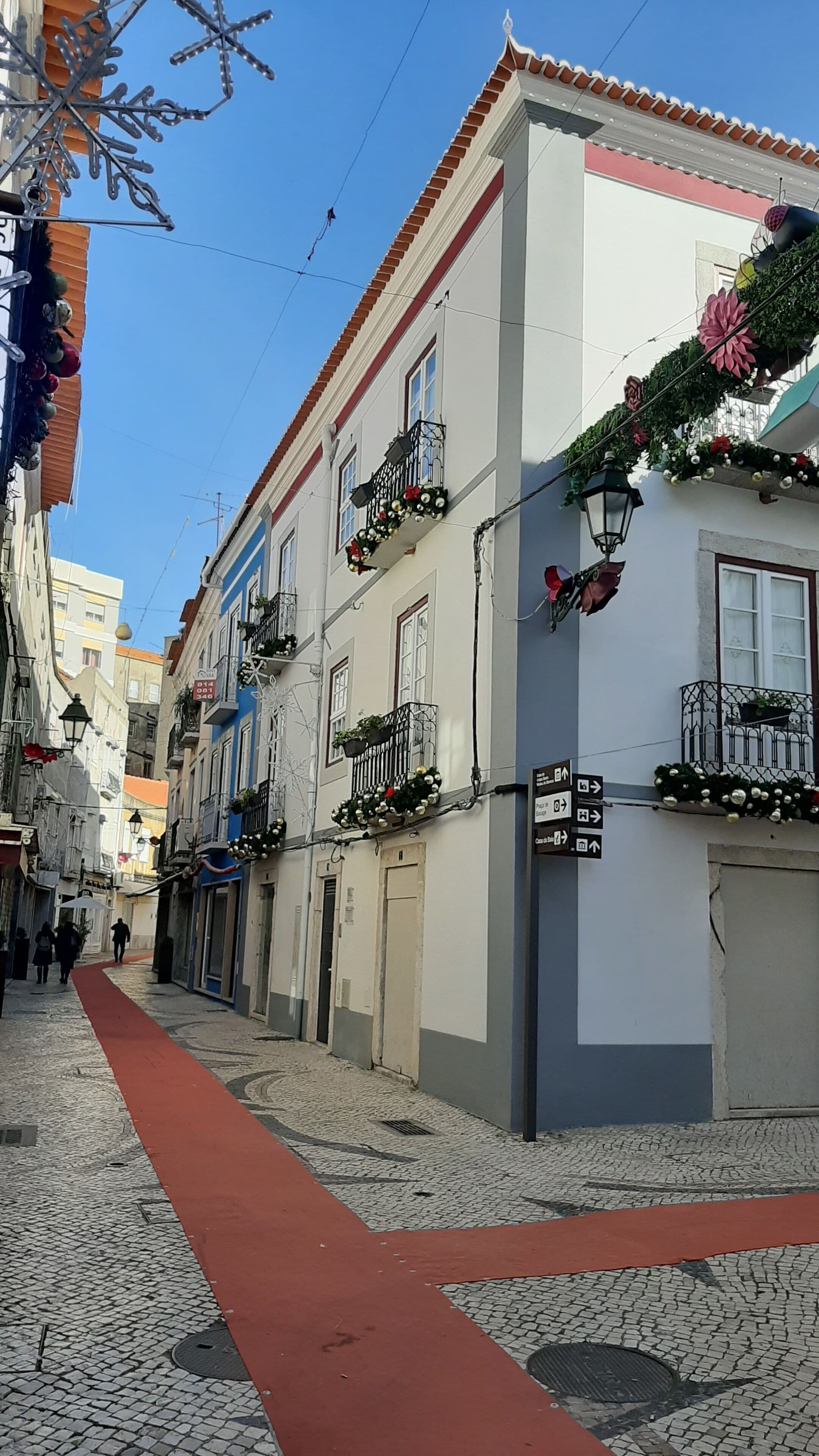 Un carrer empedrat i estret amb edificis que tenen balcons amb jardineres i decoracions penjants.