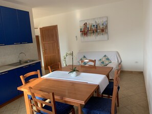 A dining area with a wooden table, blue chairs, a white tablecloth, and a painting on the wall.