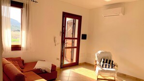 Une pièce avec un canapé rouge, un fauteuil, une porte en bois et une vue sur l’extérieur.