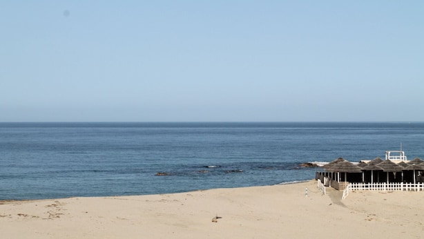Une plage avec une clôture blanche, un petit bateau et un ciel dégagé.