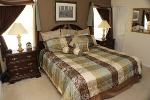 A bedroom with a large bed, two bedside tables with lamps, a dresser, a framed picture on the wall, and a mirror on the wall. - Ic051or (Kissimmee)