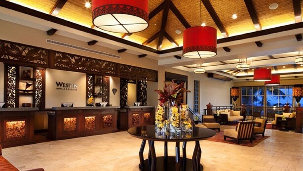 A hotel lobby with a reception desk, a round table with vases, and a high ceiling with wooden beams. - Westin Princeville 2 Bedrooms Premium Unit  (Princeville)
