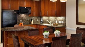 A modern kitchen with wooden cabinets, a black refrigerator, granite countertops, and a dining area with a wooden table and chairs. - Westin Princeville 2 Bedrooms Premium Unit  (Princeville)
