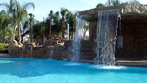A swimming pool with a waterfall feature and palm trees in the background. - 8947cp - Paradise Palms (Kissimmee)