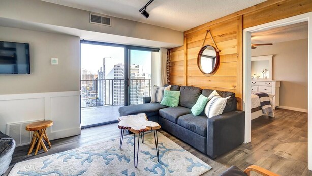 A modern apartment with a grey sofa, a round mirror, and a wooden accent wall.