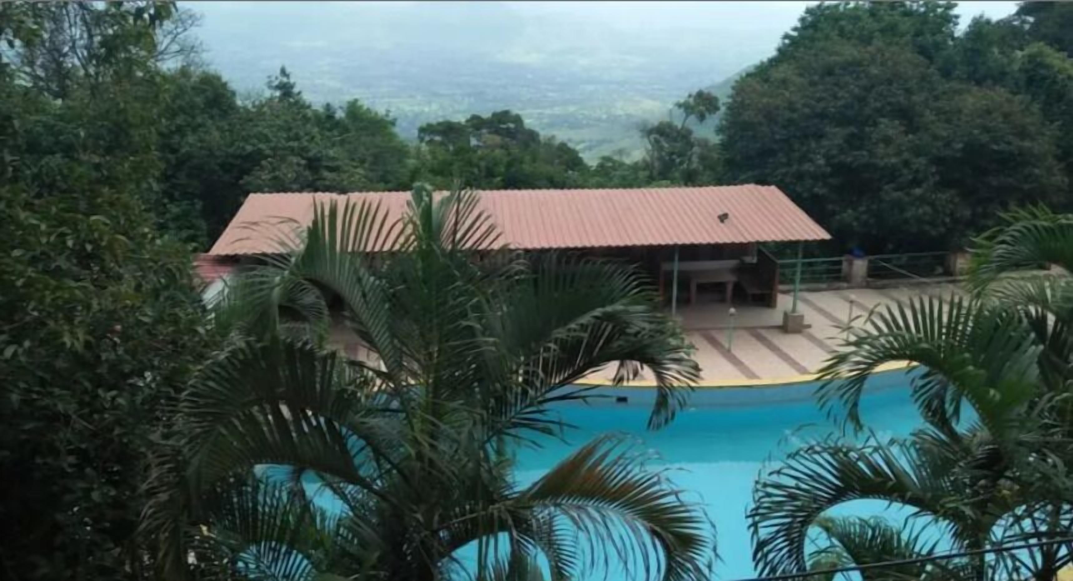 A building with a red roof, surrounded by lush greenery and a swimming pool.