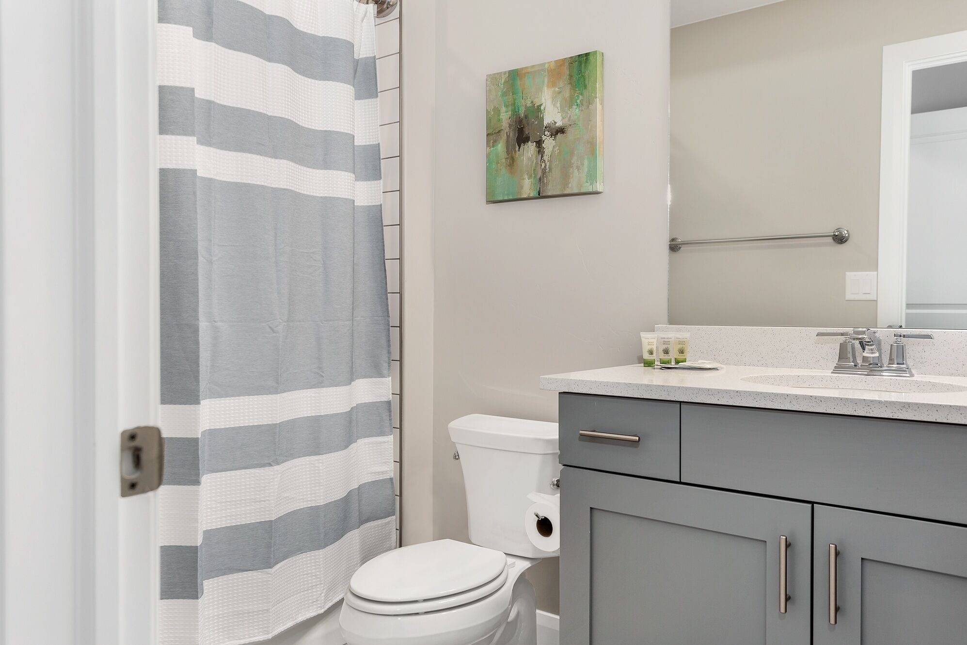 A bathroom with a striped shower curtain, a toilet, a sink with a mirror, and a painting on the wall.
