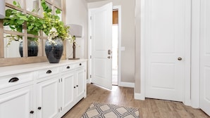 Un couloir avec des meubles blancs, un grand miroir et un vase rempli de fleurs.