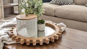 Un plateau rond en bois, sur lequel se trouve un récipient blanc perforé et une petite plante en pot, le tout posé sur une table en bois.