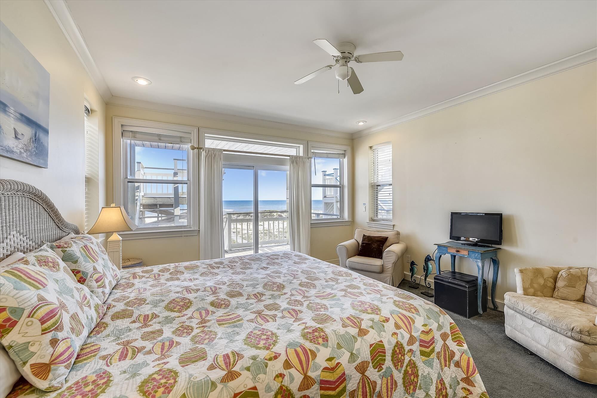 A bedroom with a bed, a chair, a television, and a view of the beach.