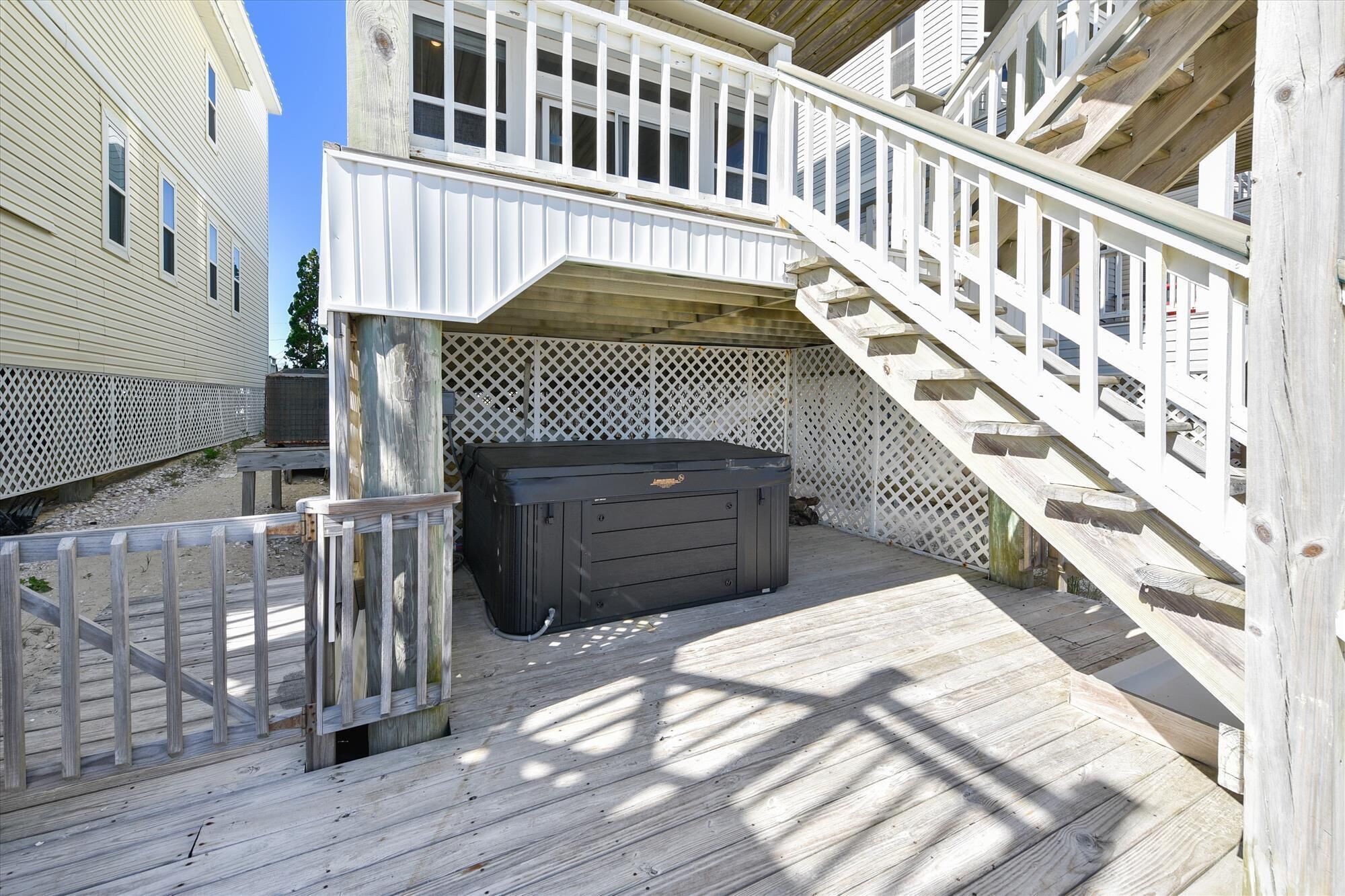A wooden deck with a hot tub, a wooden staircase, and a white fence.