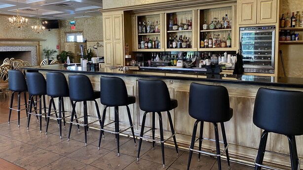 A bar area with a long counter, multiple stools, and a variety of bottles and glasses. - Blueberry Plantation Golf Resort (Alma)