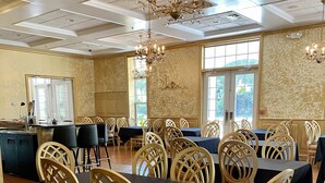 A dining area with wooden chairs and tables, a chandelier, and a view of the outdoors through large windows. - Blueberry Plantation Golf Resort (Alma)