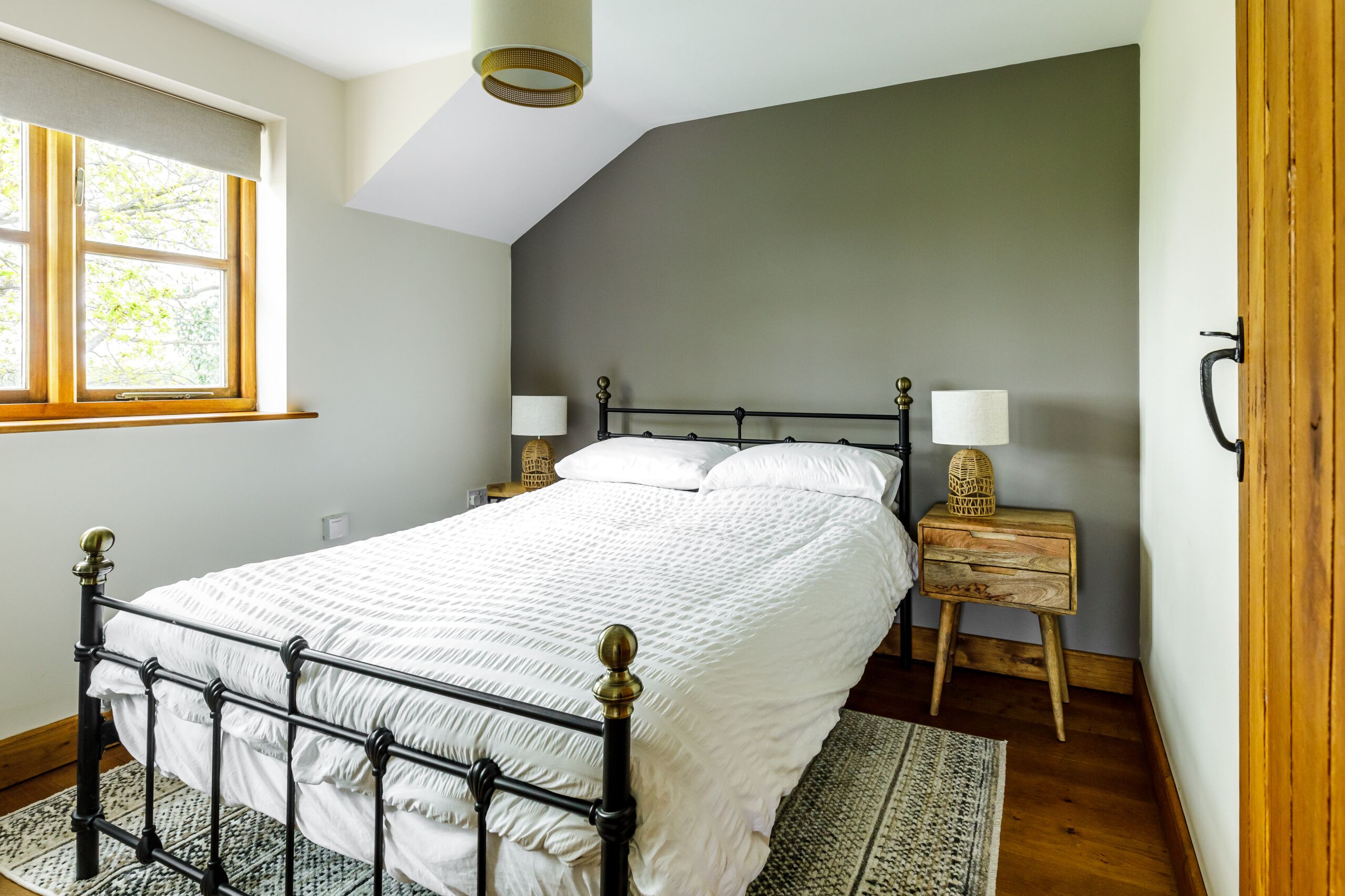 A bedroom with a bed, bedside lamps, a nightstand, a window, and a wooden door.