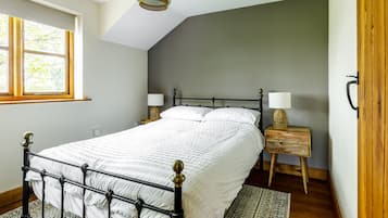 A bedroom with a bed, bedside lamps, a nightstand, a window, and a wooden door.