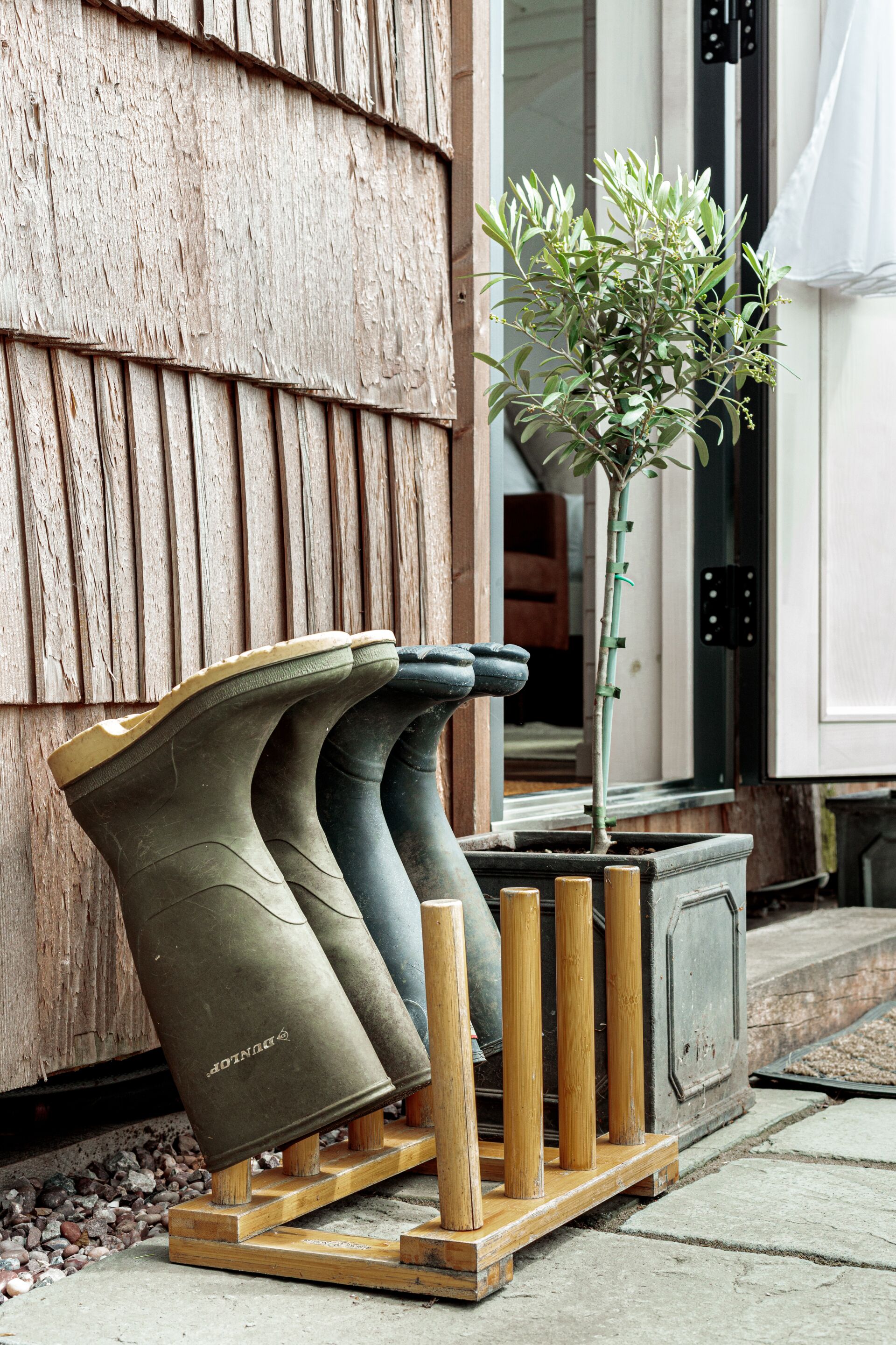 A pair of boots on a wooden stand with a potted plant beside a wooden door.