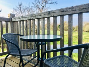 A wooden deck with a glass table and two wicker chairs.