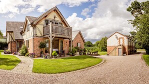 A large, two-story house with a balcony, surrounded by a well-maintained lawn and gravel driveway. - Oak Mead (Wrexham)