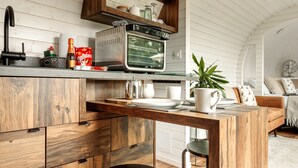 A kitchen with wooden cabinets, a built-in microwave, and a wooden dining table with a black chair. - Oak Mead (Wrexham)