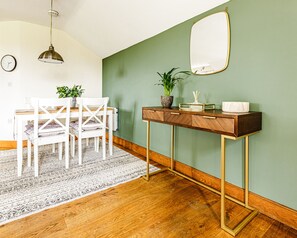 A dining area with a wooden table, white chairs, a green wall, a mirror, and a hanging light fixture.