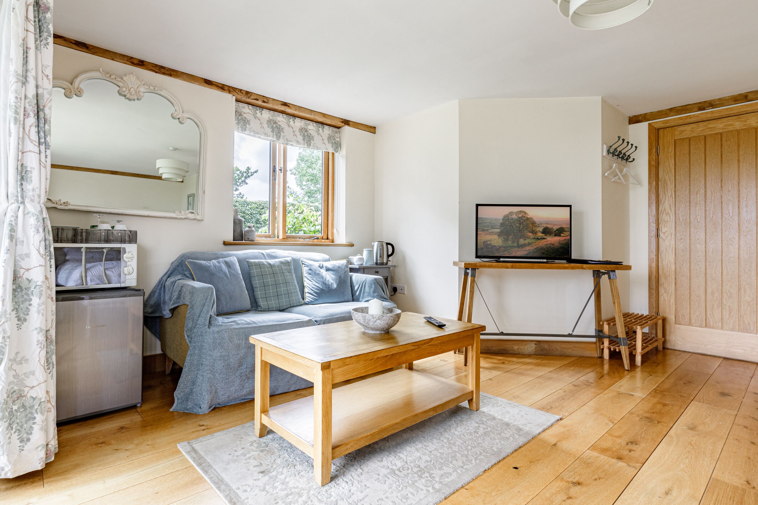 A cozy living room with a sofa, a coffee table, a television on a stand, and a wooden floor.