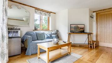 A cozy living room with a sofa, a coffee table, a television on a stand, and a wooden floor.