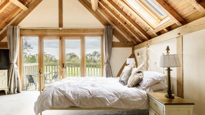 A bedroom with a wooden ceiling, a large window, a bed, a nightstand, and a view of the outdoors. - Oak Mead (Wrexham)