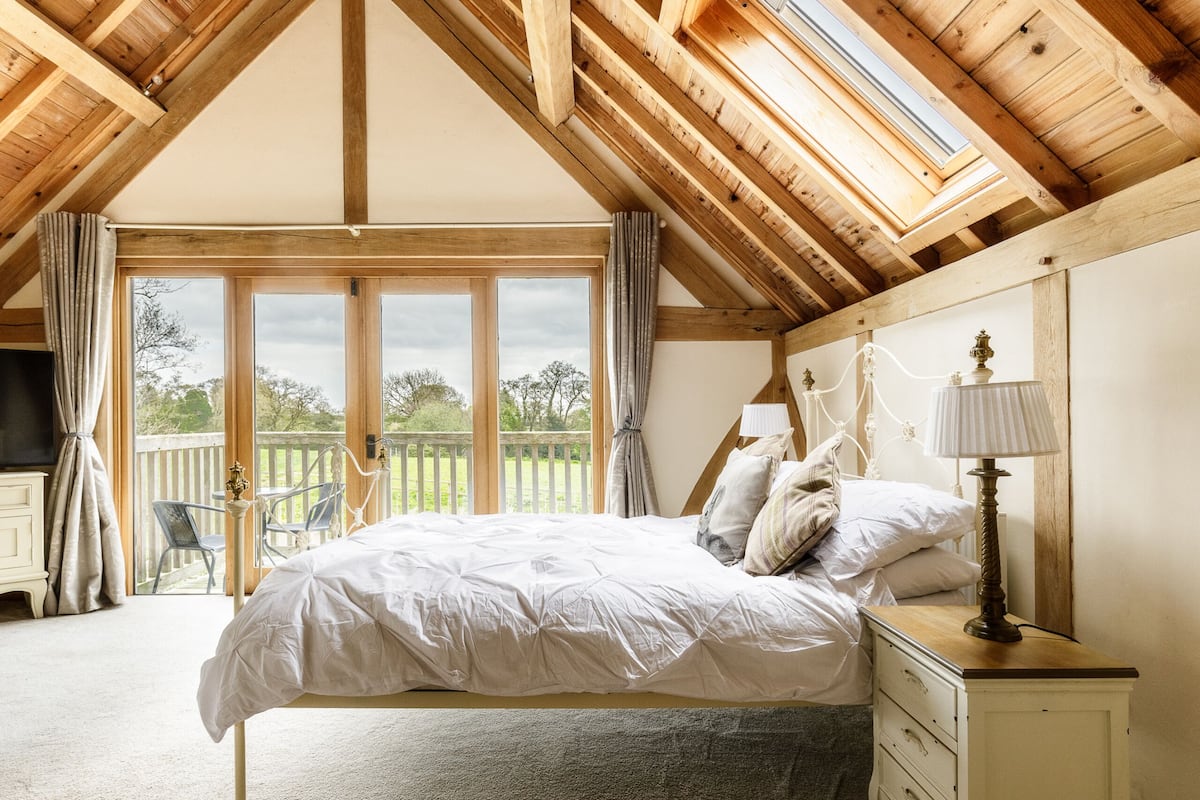 A bedroom with a wooden ceiling, a large window, a bed, a nightstand, and a view of the outdoors.