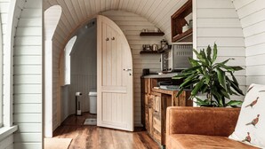 A cozy living room with a wooden floor, a brown sofa, and a coffee table. There is a kitchen area with wooden cabinets and a microwave. - Oak Mead (Wrexham)