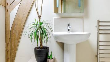 A bathroom with a white pedestal sink, a wooden bench, a potted plant, and a wooden ceiling beam.