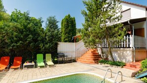 A swimming pool with a tiled edge, surrounded by lounge chairs and a staircase leading to a white fence.