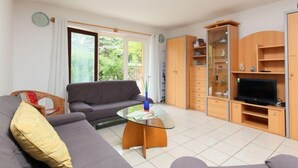 A living room with a grey sofa, a glass coffee table, a TV stand, and a wooden cabinet.