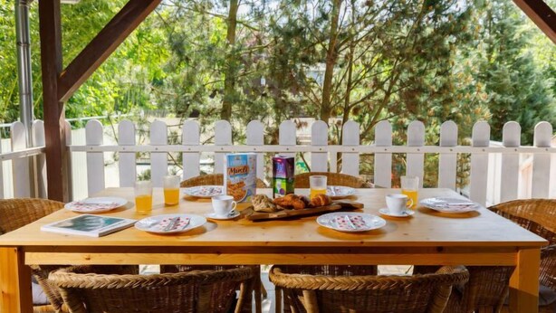 A wooden table with breakfast items, wicker chairs, and a white picket fence in the background.
