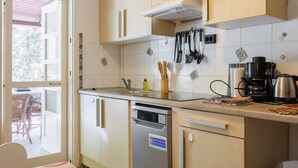A kitchen with light wooden cabinets, a dishwasher, a coffee maker, and various utensils hanging on the wall.