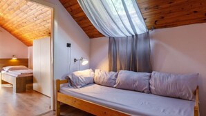 A cozy bedroom with a wooden ceiling, a single bed, a bedside lamp, and a window with curtains.