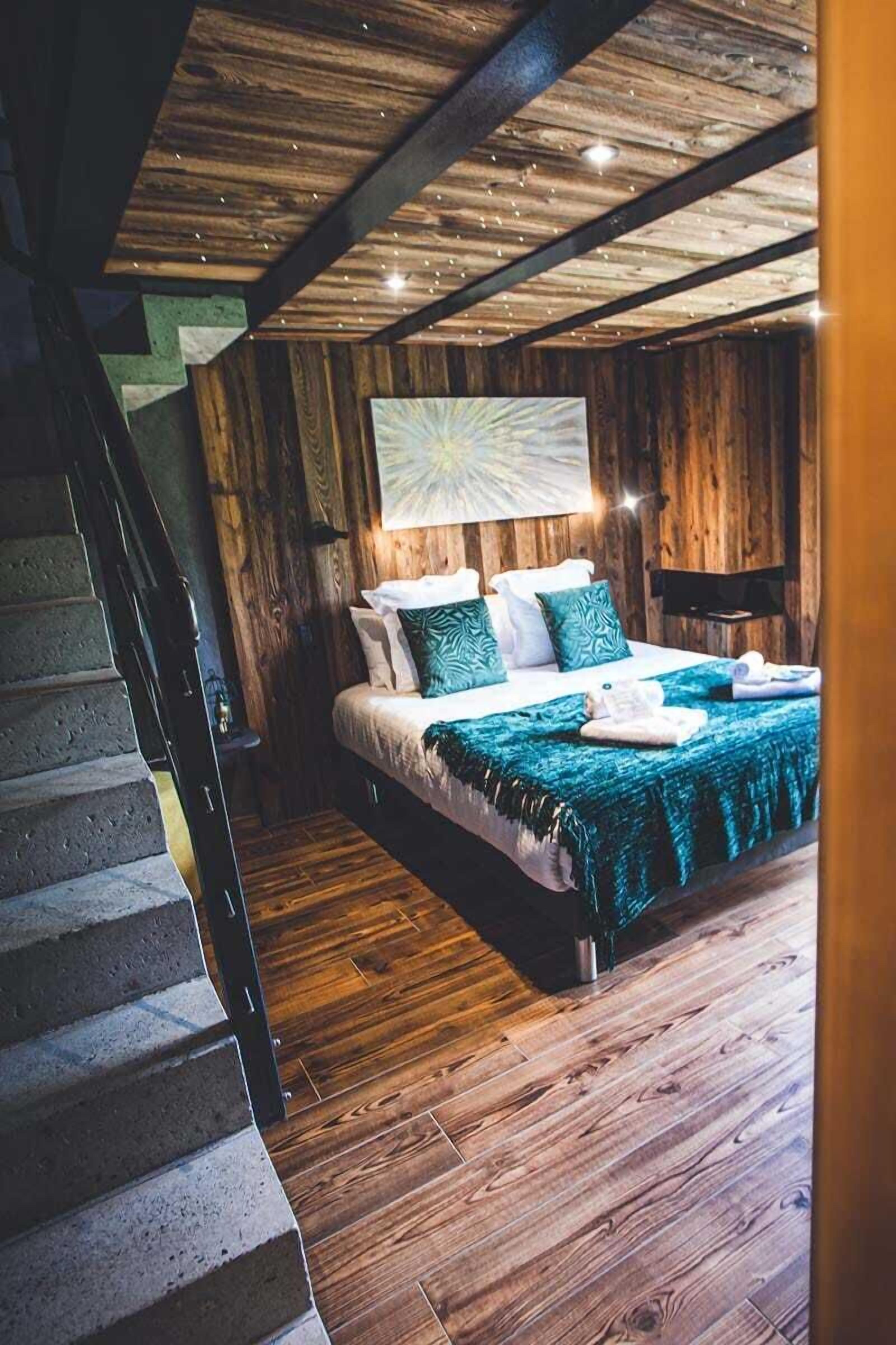 A bedroom with a wooden ceiling, a bed with a green blanket, and a painting above the bed.