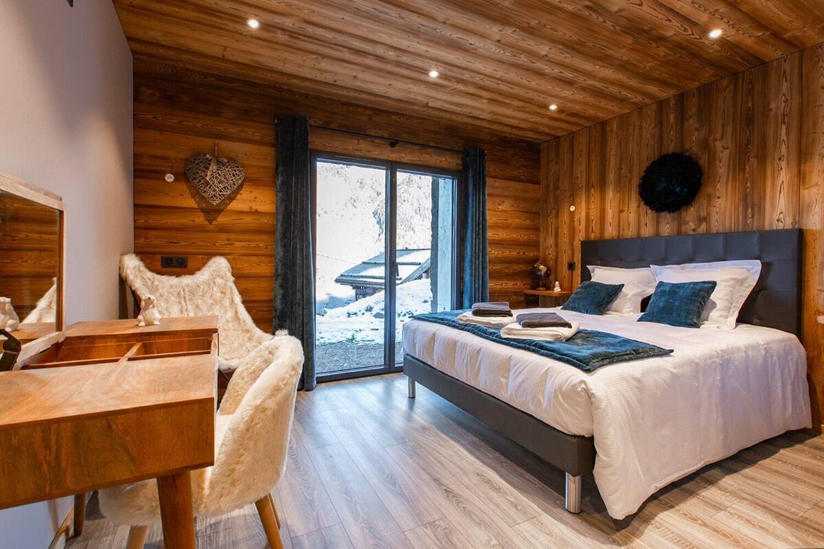 A modern log cabin bedroom with a large bed, a wooden desk, and a chair.