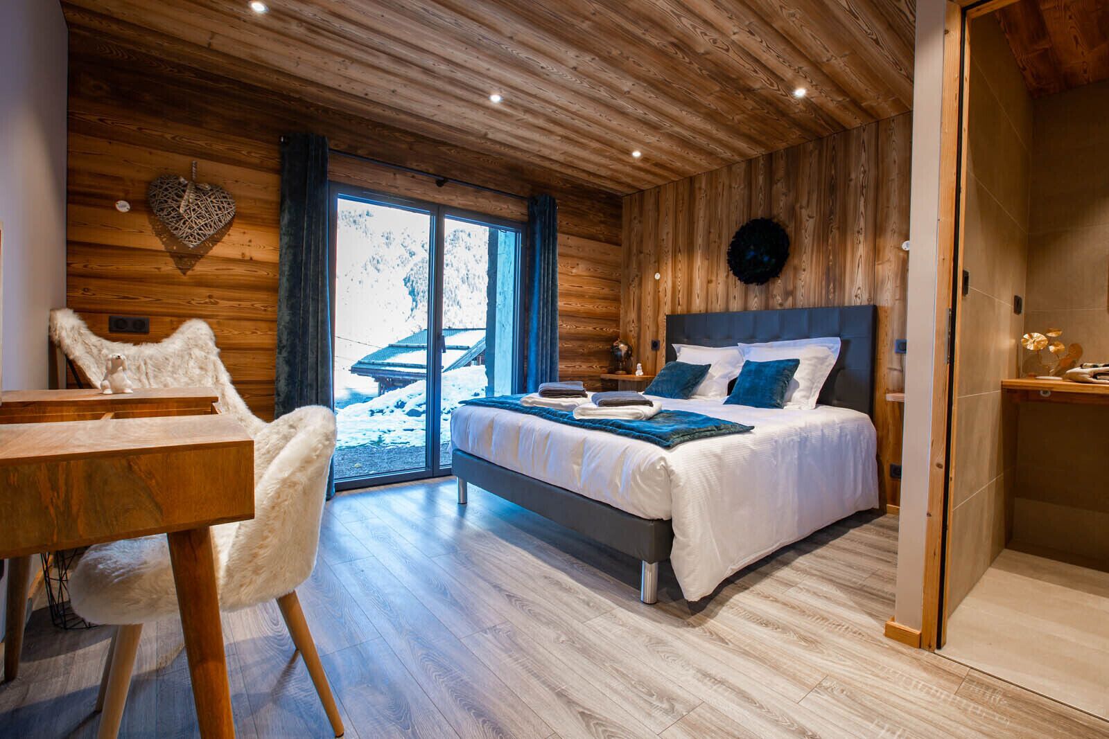 Ein modernes Schlafzimmer mit einem großen Bett, Holzwänden und Blick auf eine verschneite Landschaft.