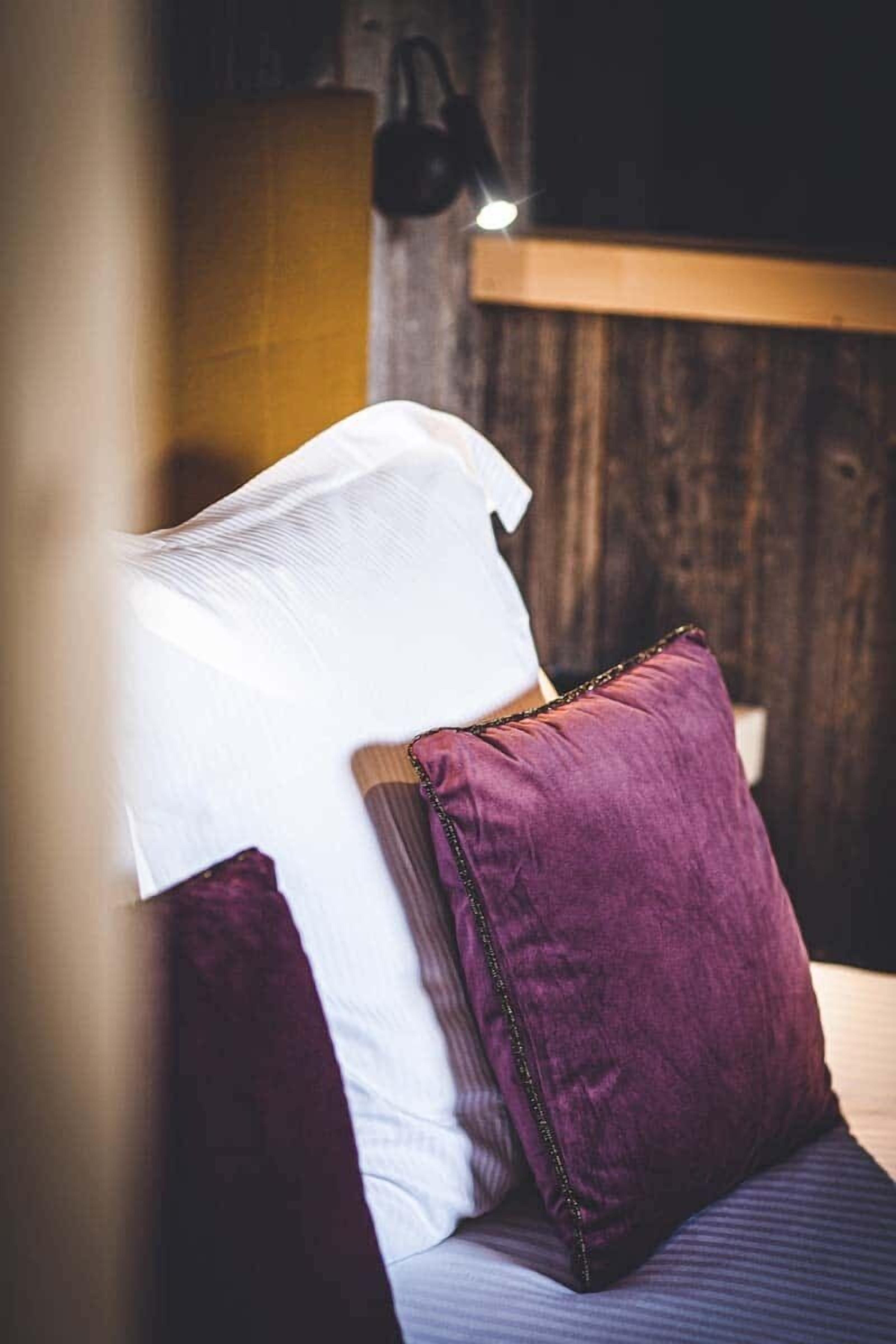 Un lit avec des oreillers blancs et violets, une tête de lit en bois et une lampe suspendue.