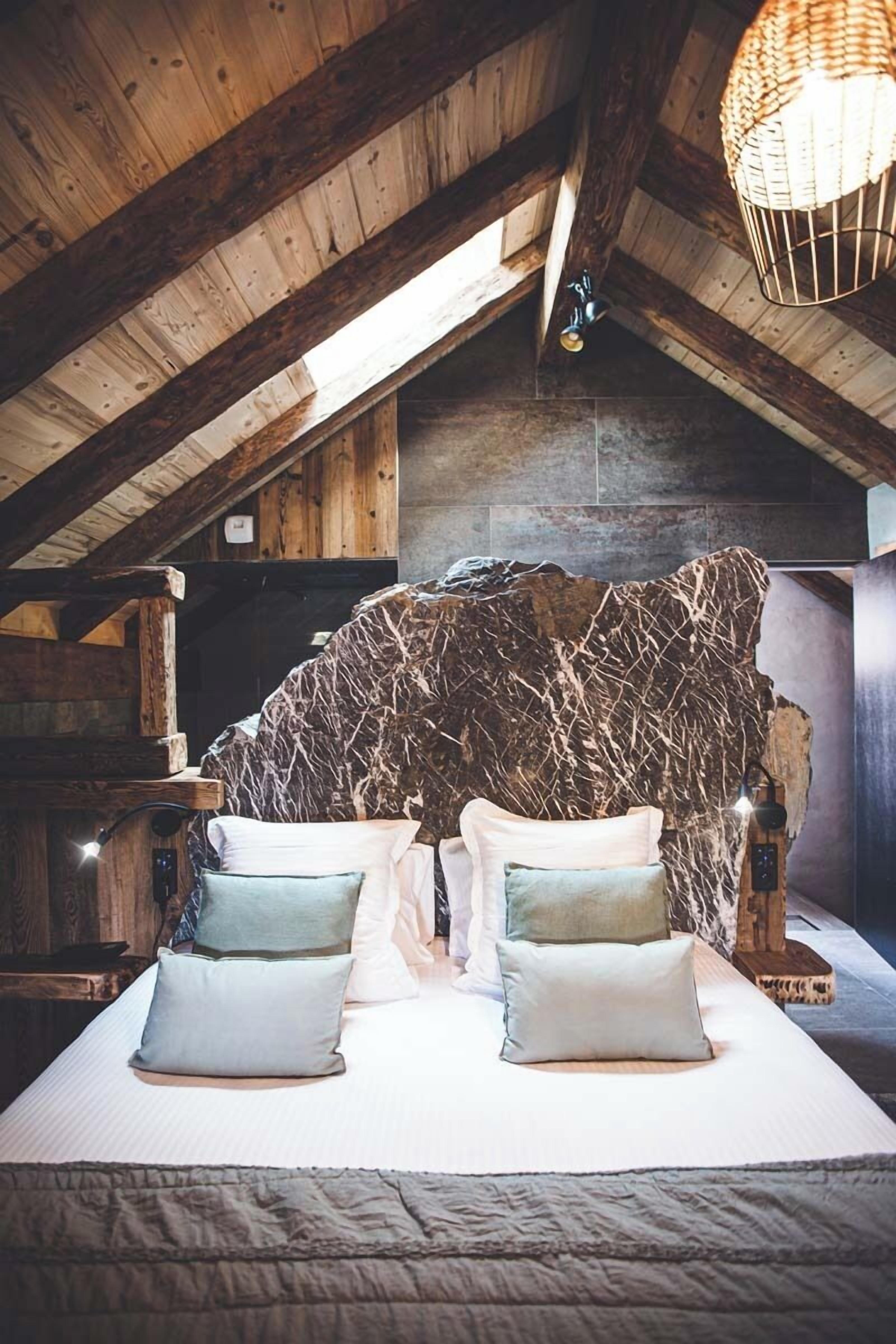 Een rustieke slaapkamer met een stenen hoofdbord, een bed met twee kussens en een houten plafond.