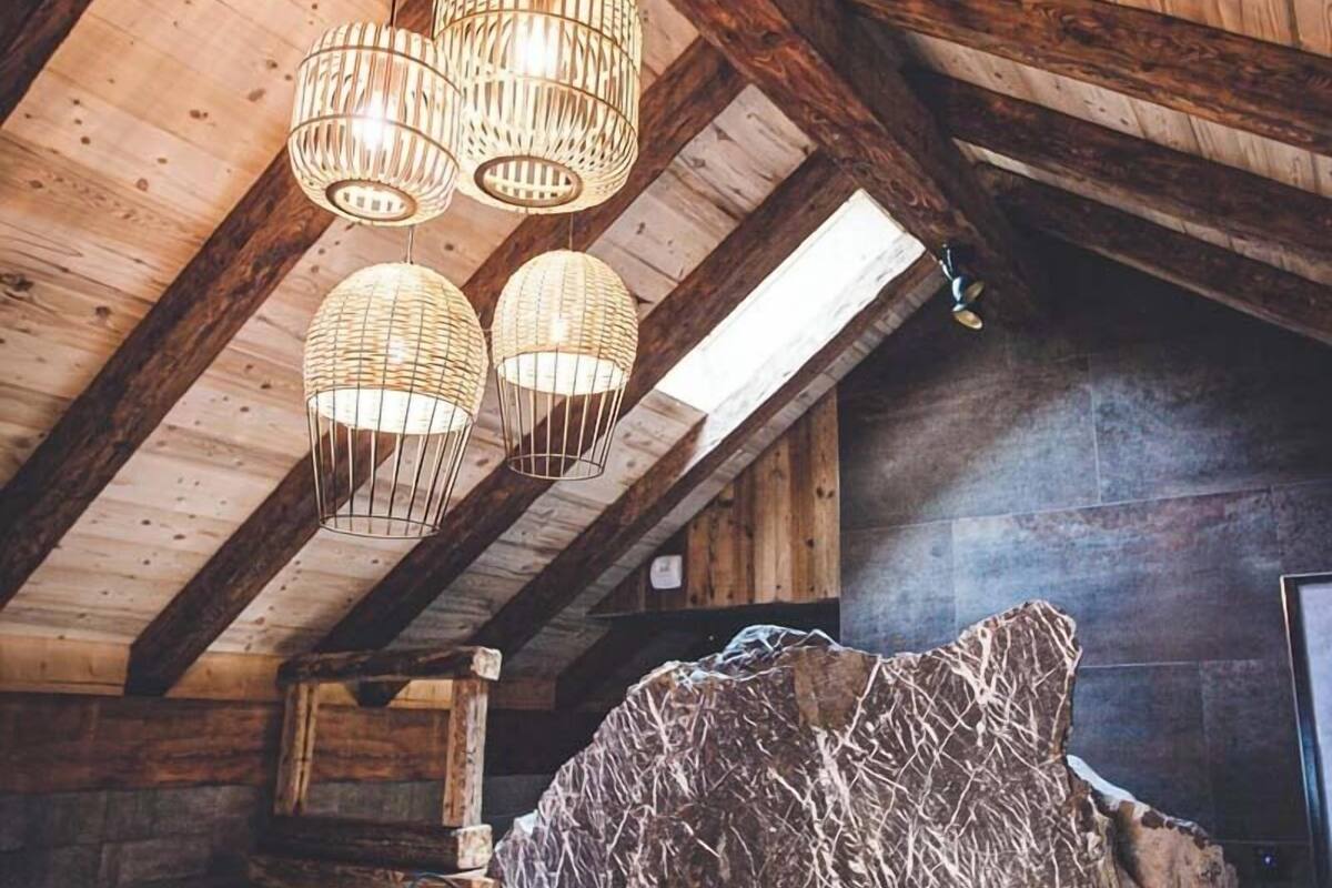 A rustic bedroom with a wooden ceiling, a large bed with multiple pillows, and a stone headboard.