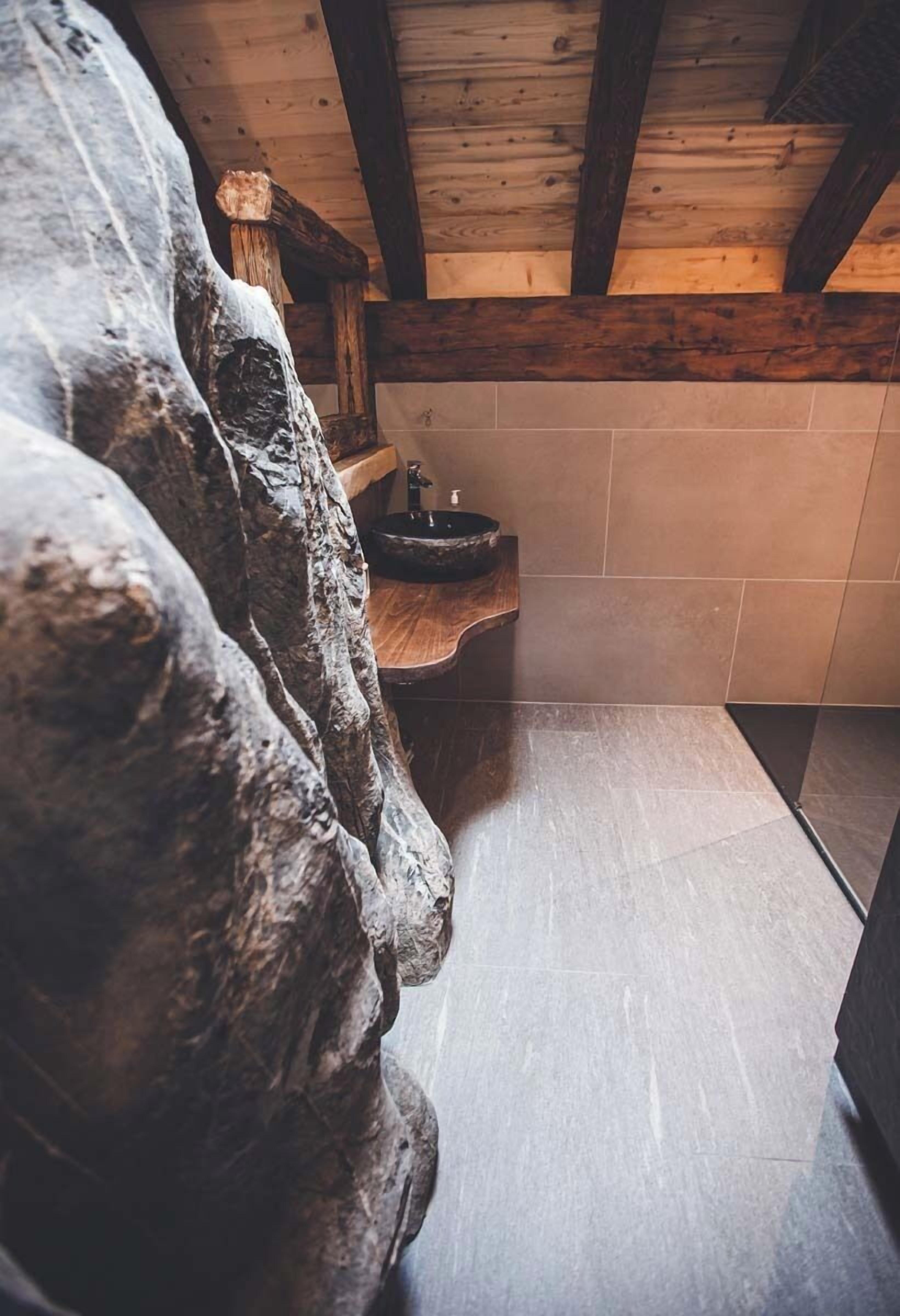 Een badkamer met een stenen muur, houten balken en een wastafel.