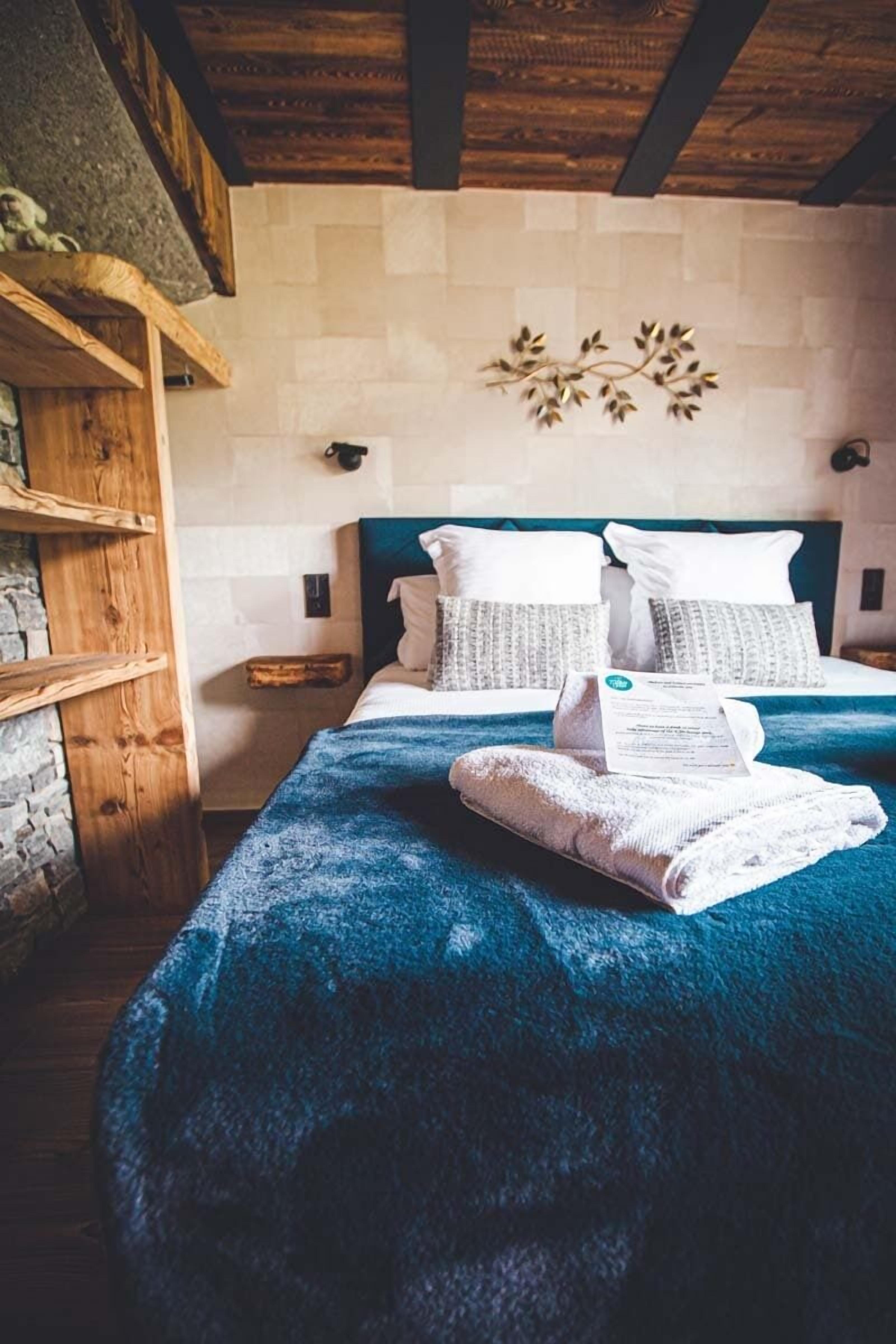 A bedroom with a bed, wooden headboard, stone wall, and a decorative wall piece.