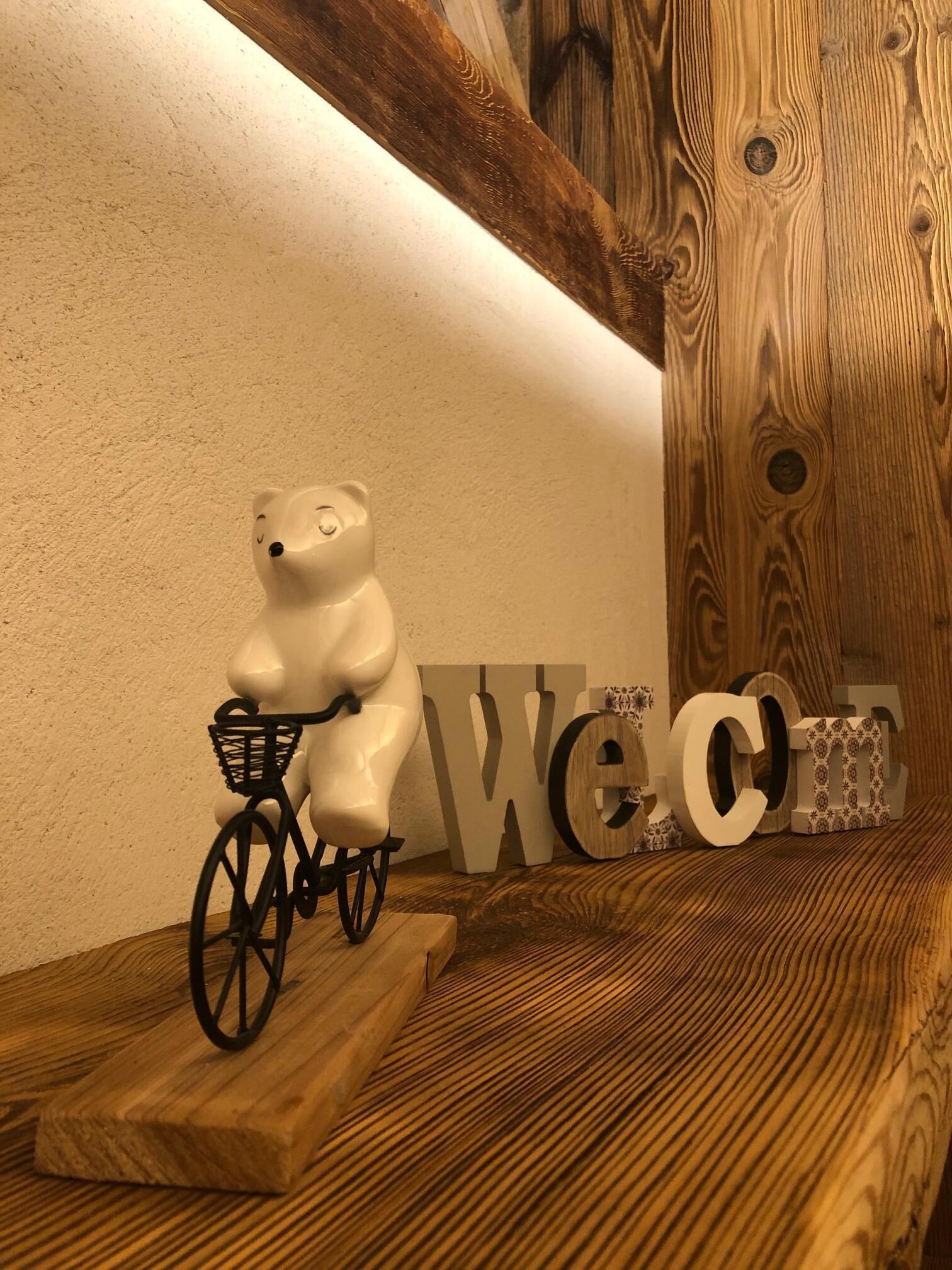 Un banc en bois orné d’une figurine d’ours blanc à bicyclette, une pancarte « Bienvenue » et un mur en bois.