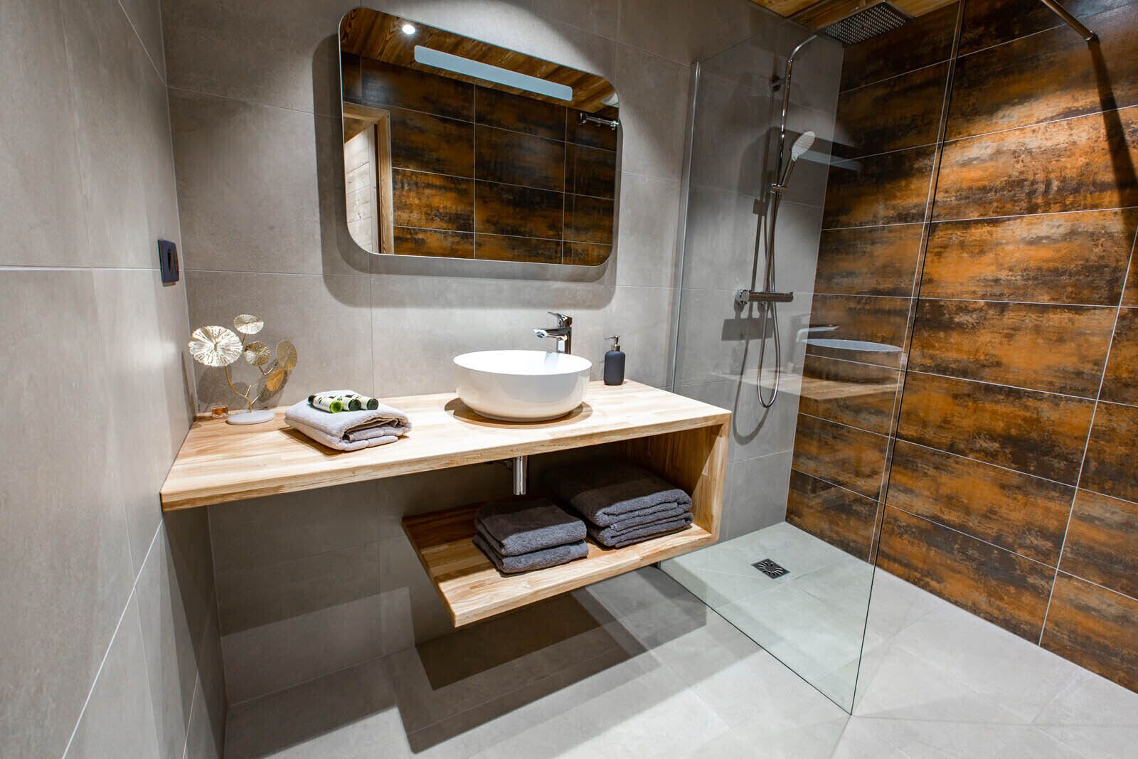A modern bathroom with a wooden vanity, a large mirror, a round sink, and a glass-enclosed shower.