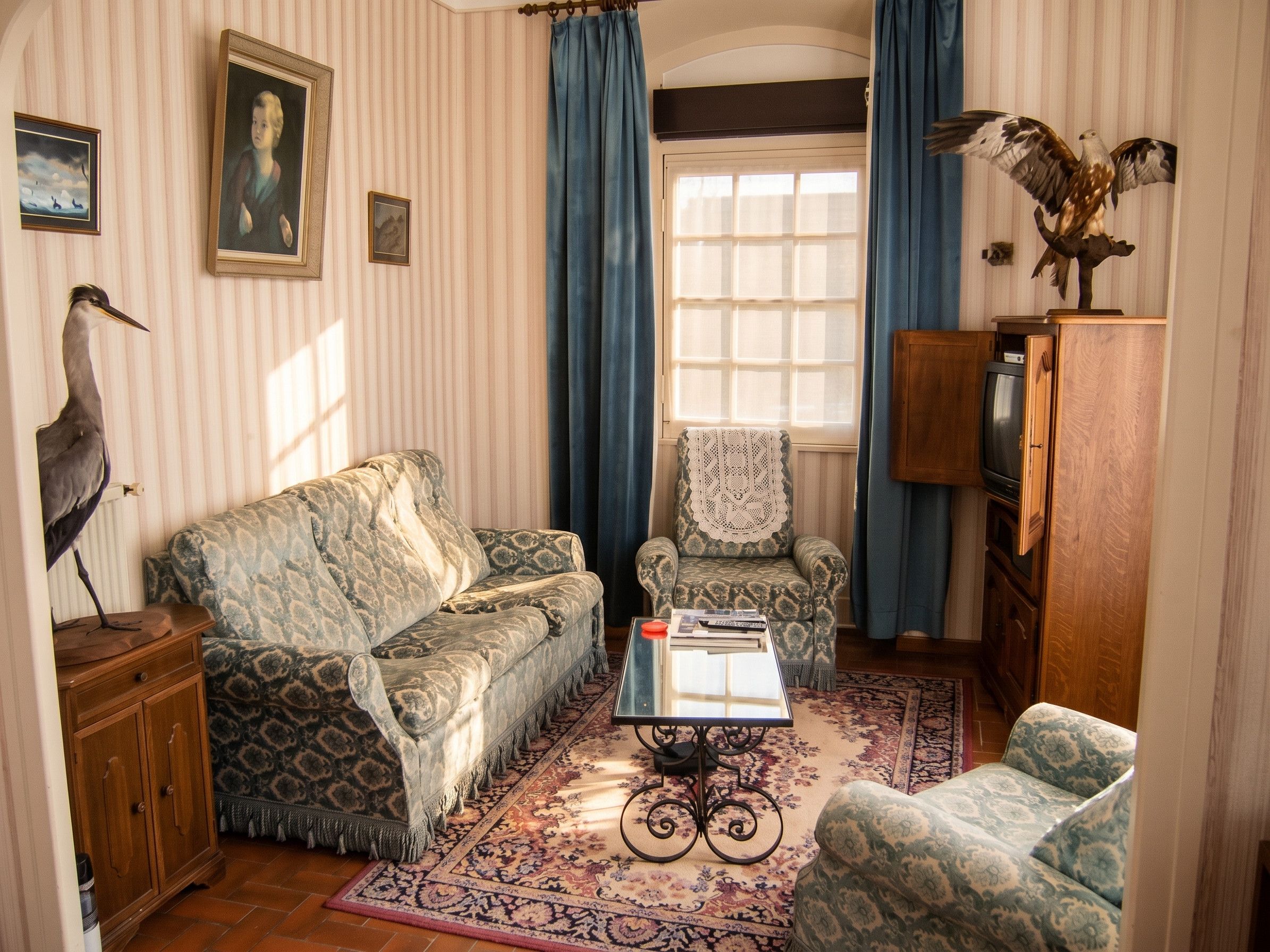 Een woonkamer met een gestreept bankstel, een bijpassende fauteuil, een salontafel, een houten kast en een televisie.