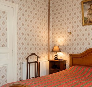 Un dormitorio con cama, mesita de noche con lámpara, silla y radiador.