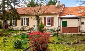 A house with a red-tiled roof, a garden with various plants and flowers, and a green door.
