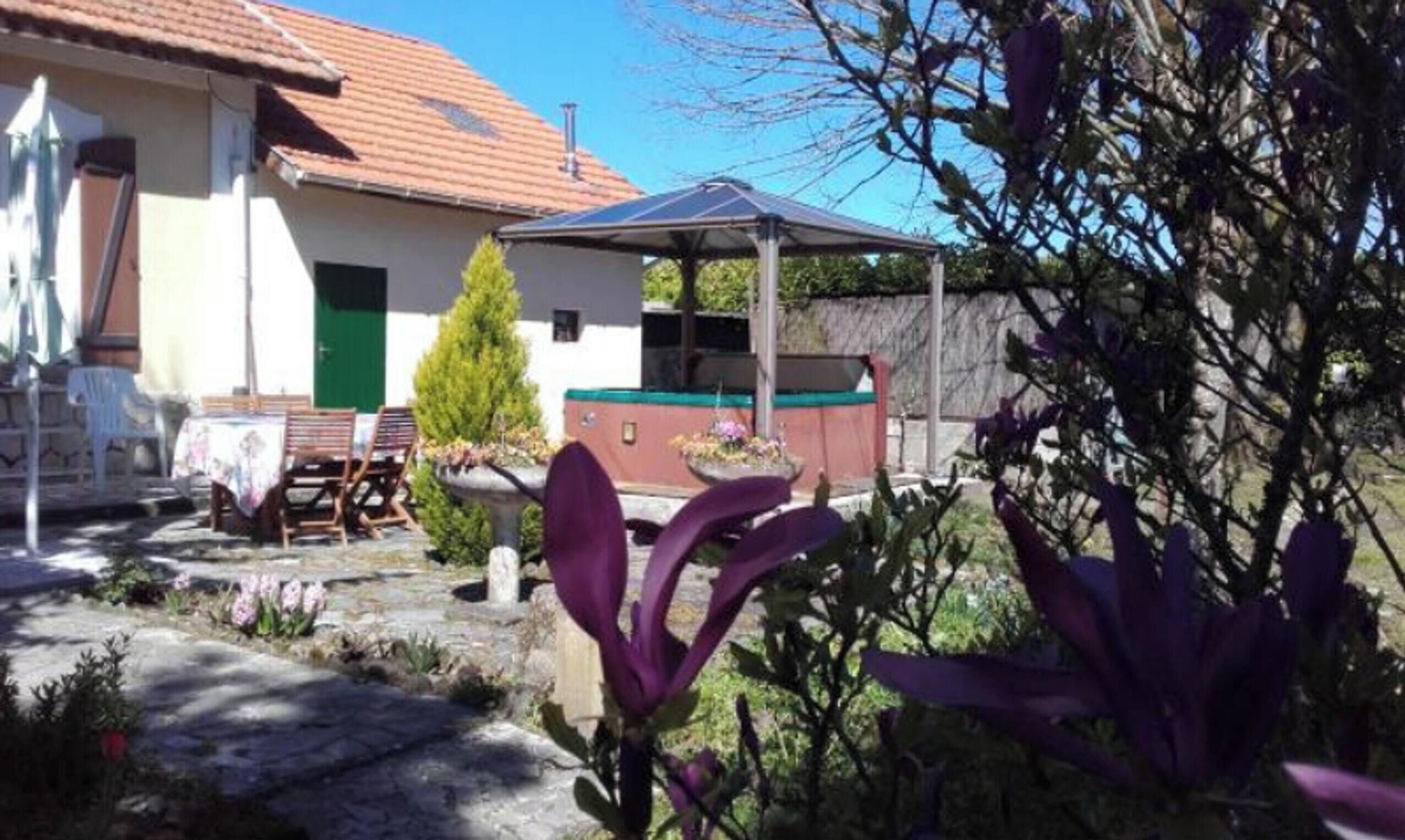 Una casa con un patio, una porta verde e un piccolo giardino con fiori viola.