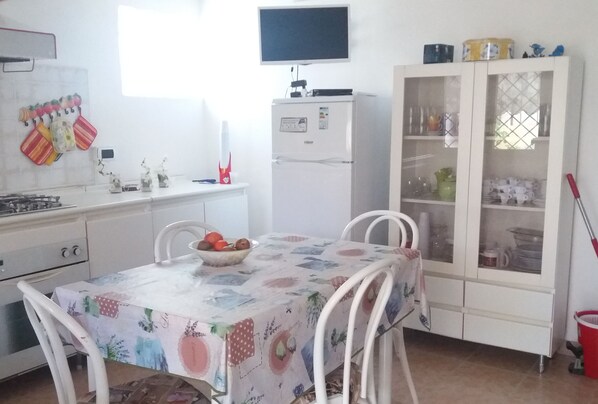 A kitchen with a refrigerator, a dining table with chairs, a cabinet with glass doors, and a window.